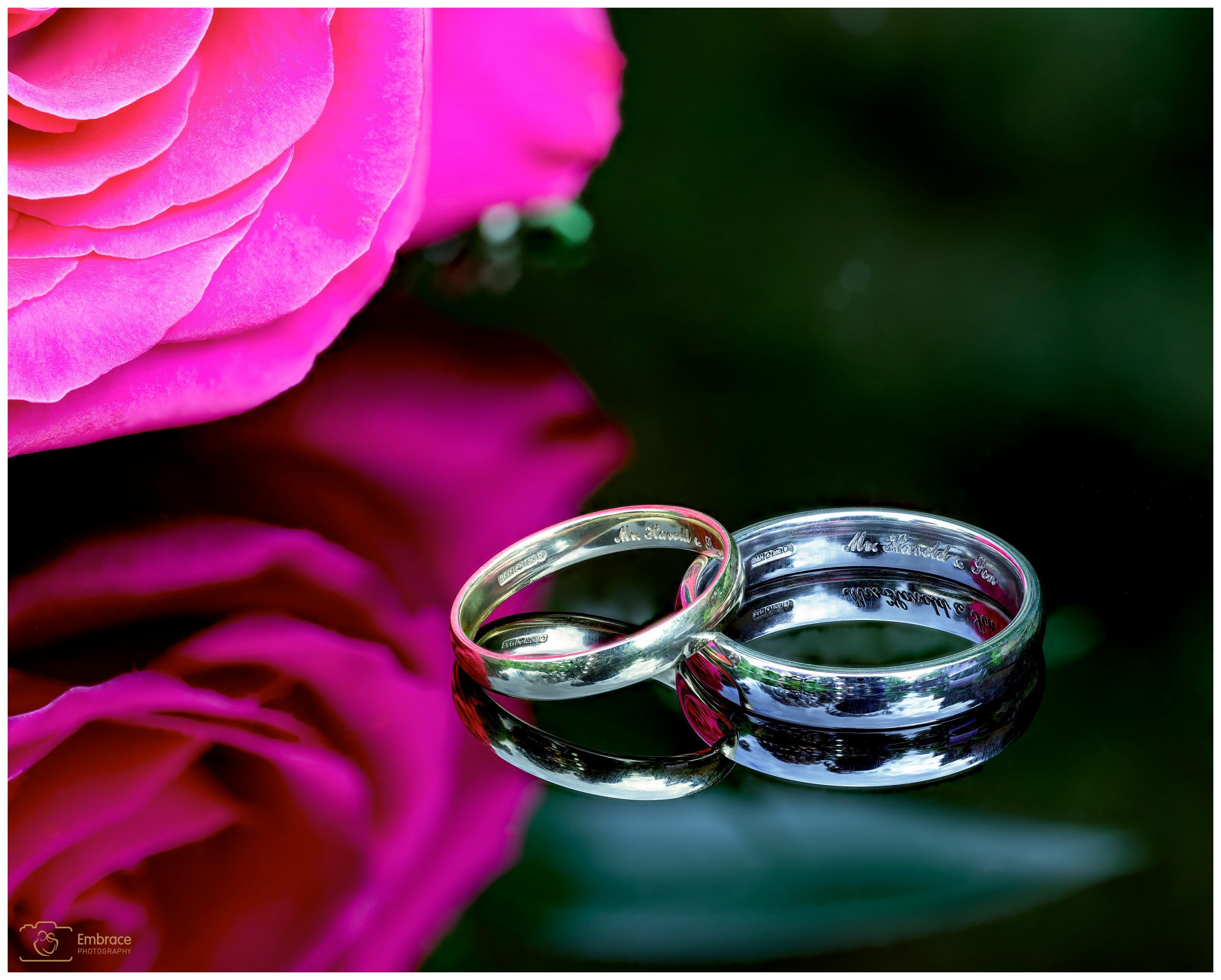 Detailed photo of the bride and groom's wedding band with a buttonhole in the background.